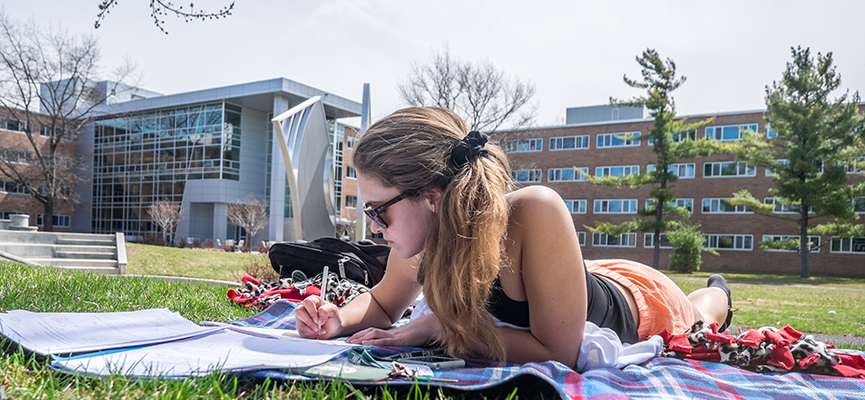 Photo of a girl studying outside while laying on a blanket