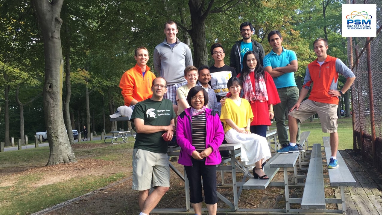 A group photo of MSIM students, Peiru Wu, and Keith Primslow sitting and standing on bleachers next to a baseball field at a park.